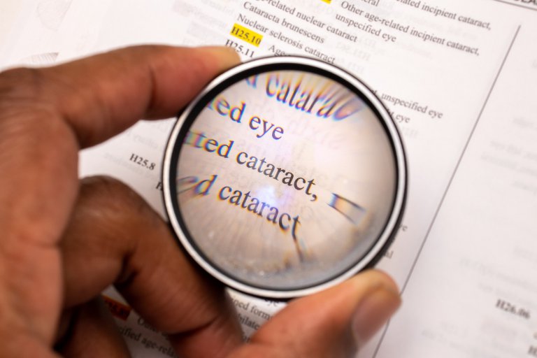 African American man with magnifying glass looking at the word cataract in a book